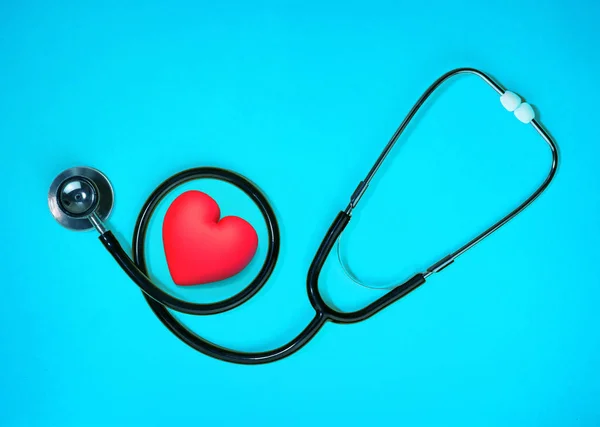 Gezondheidsonderzoek met rood hart en stethoscoop op blauwe achtergrond. — Stockfoto