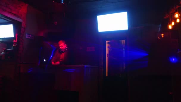 DJ spielt im Nachtclub, der von buntem Licht erleuchtet wird. — Stockvideo