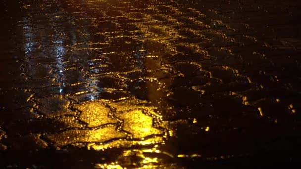 Regen auf der nächtlichen Straße. Gelbe Lichtreflexion in Pfütze. — Stockvideo