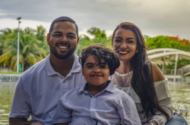 Bir çift Latin Amerikalı erkek ve kadın, oğlanla birlikte otizmden muzdaripler, bir portre ailesinde mutlular, parkta birlikte gülüyorlar, sarılıyorlar