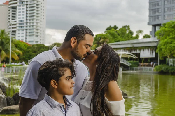 Para mężczyzn i kobiet z Ameryki Łacińskiej, z chłopcem cierpi na autyzm, szczęśliwy w rodzinie portret na świeżym powietrzu razem w parku, trzech śmiech przytulanie — Zdjęcie stockowe