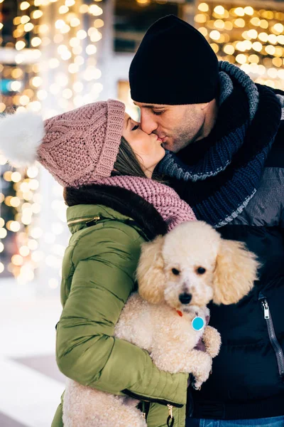 Young loving couple at the street with their dog with christmas lights on background