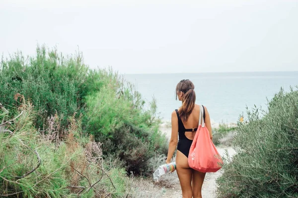 Back view of woman in bikini with bag walking on wild beach