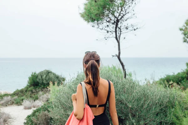 Back view of woman in bikini walking on wild beach