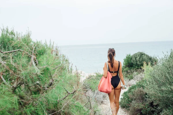 Back view of woman in bikini walking on wild beach