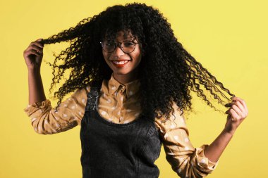 Afro saçlı, gözlüklü ve sarı arka planlı genç Afrikalı Amerikalı.