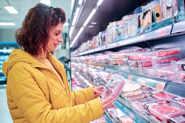 Genç bir kadın süpermarketin raflarından et alıyor.