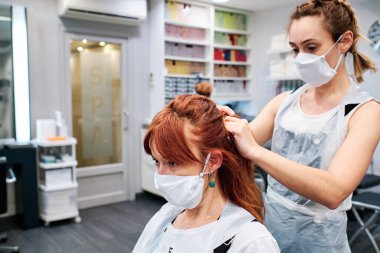 Güzellik salonundaki kuaför. Coronavirüs salgınından korunmak için maske takıyor. Sosyal uzaklık kavramı.