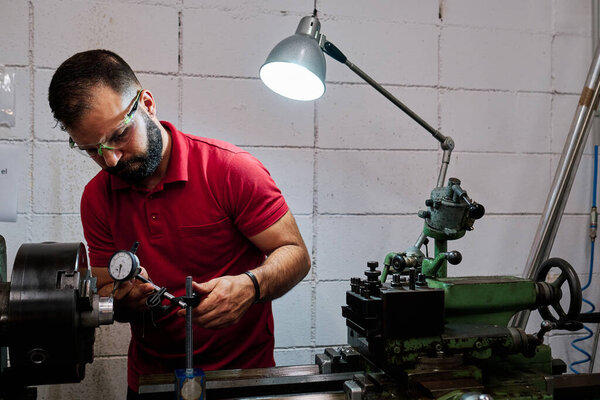 Работник крупного плана в форме и защитных очках, работающий на точильном станке
