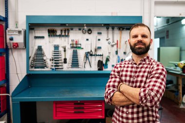 Yetişkin bir adam atölyesinin önünde arkasında bir sürü aletle.