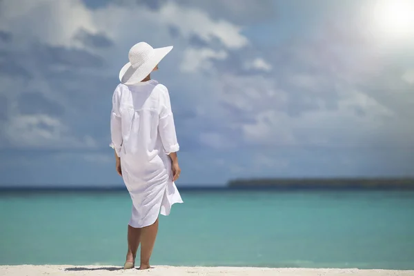 Elegant young woman in a hat standing on beach — Stock Photo, Image