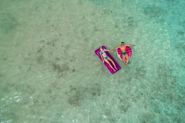 Summer holiday fashion concept - tanning couple at the beach on a turquoise sea shot from above. Top view from drone. Aerial view of slim woman and man sunbathing lying on a beach in Thailand.