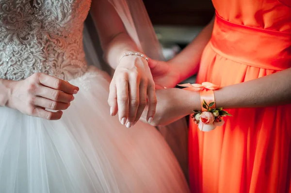 Подружка невесты в оранжевом платье помогает невесте носить браслет — стоковое фото