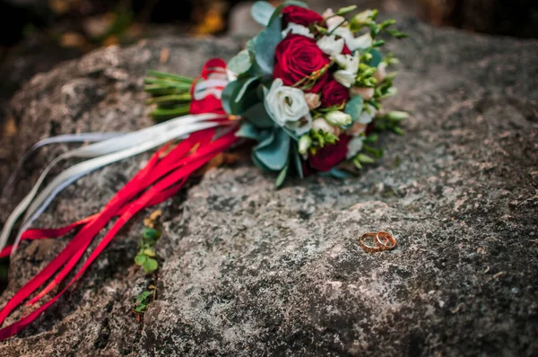 Ramo de rosas y anillos de boda dorados yacen en la piedra —  Fotos de Stock