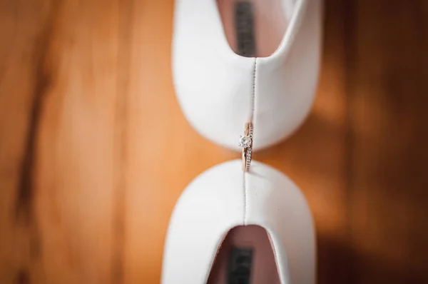 Gouden diamanten ring tussen paar witte hoge hak schoenen — Stockfoto