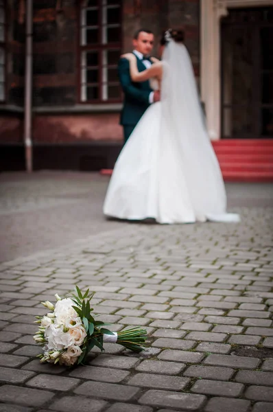 Par de noivo e noiva no foco traseiro e buquê de flores fica no pavimento — Fotografia de Stock