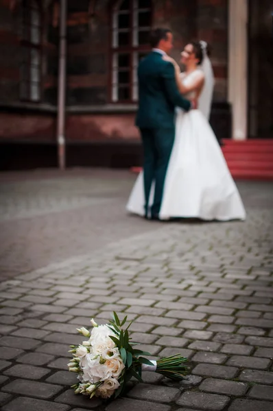 Pair of groom and bride on the back focus and bouquet of flowers lies on the pavement — Stock Photo, Image