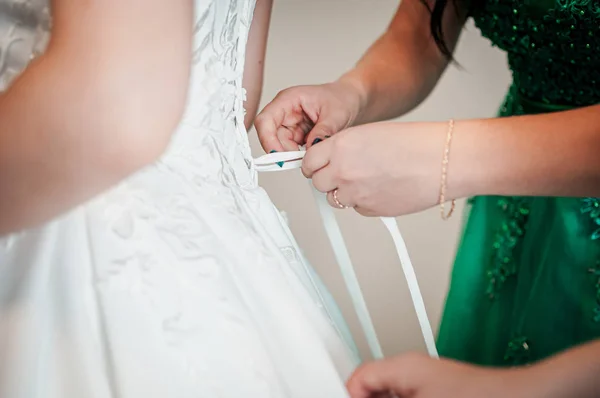 Bridesmaids assist bride to wear wedding dress — Stock Photo, Image