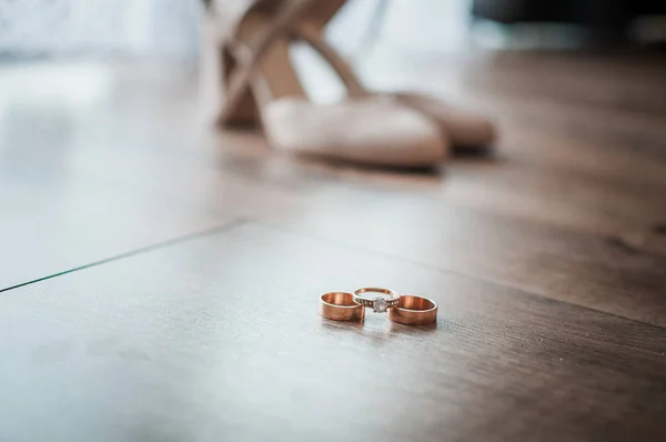 Três anéis de casamento de ouro e sapato de salto alto branco na mesa — Fotografia de Stock
