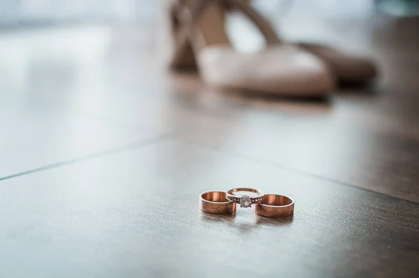 Três anéis de casamento de ouro e sapato de salto alto branco na mesa — Fotografia de Stock