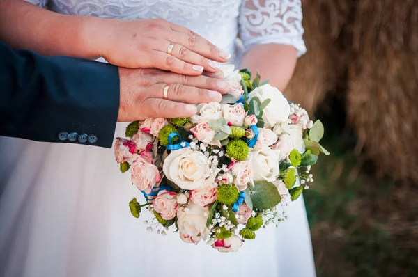 Handen van bruidegom en bruid liggen op het boeket bloemen — Stockfoto