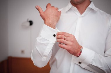 Gömleğe kol düğmesi takan bir adam.