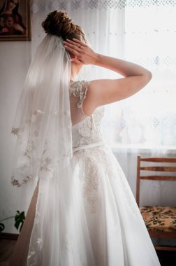 Bride with bridal veil standing near the window clipart