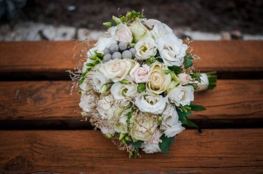 Kahverengi bir bankta beyaz bir buket çiçek yatıyor.