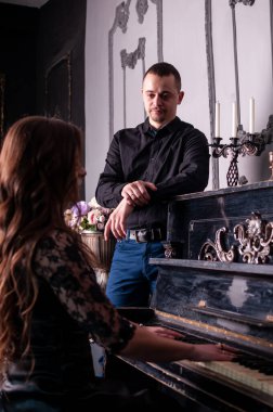 Kadın piyanoda çalarken, erkek yanında duruyor.