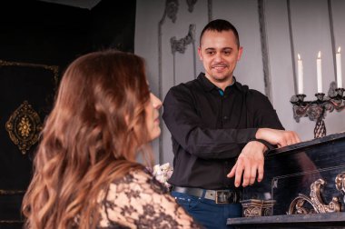 Kadın piyanoda çalarken, erkek yanında duruyor.