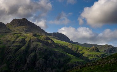 Fırtınalı gökyüzü ve parlak bir güneş ışığı İngiliz Gölü Bölgesi 'ndeki Langdale Pikes' in üzerinde.