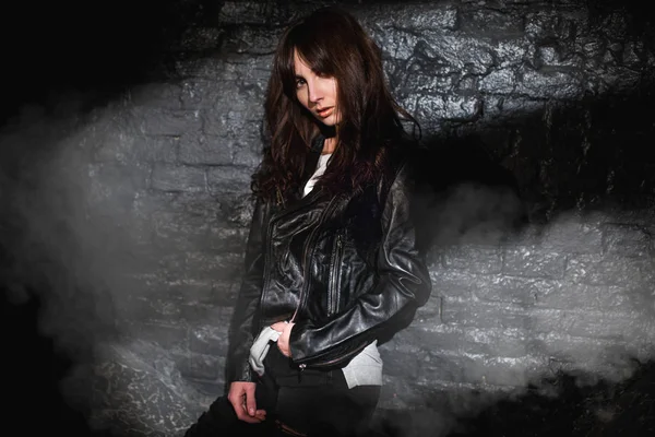 Bella donna nella giacca di pelle contro il muro di mattoni di buio — Foto Stock