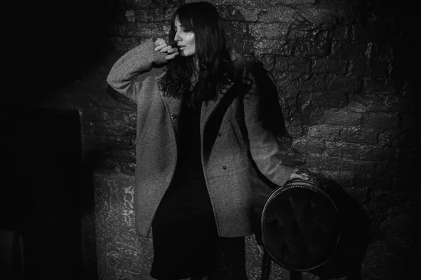 Bella donna in un cappotto grigio su un muro di mattoni scuri — Foto Stock