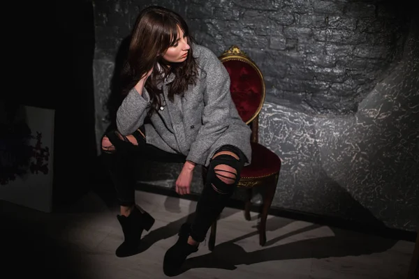 Beautiful woman in a gray coat on a dark brick wall — Stock Photo, Image