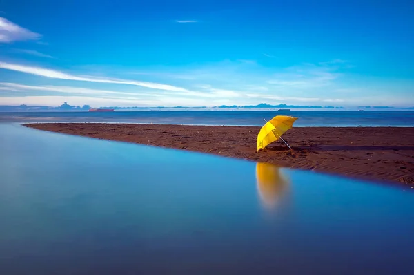 Sahilde kıyıya vurmuş bir şemsiye. Deniz manzarası ve açık gökyüzü var.