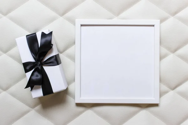 Marco de imagen vacío con un regalo con lazo negro sobre tufti blanco — Foto de Stock