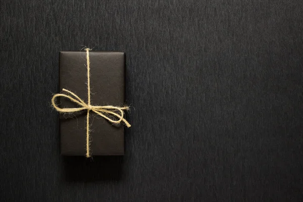 黒い背景に弓で黒い紙に包まれたプレゼント — ストック写真