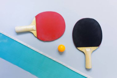 Masa tenisi pinpon oyuncakları kırmızı ve siyah raketler, turuncu top, mavi arka planda mavi ağ..