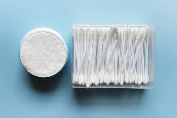 Cotton pads with cotton swabs in plastic box on blue background.