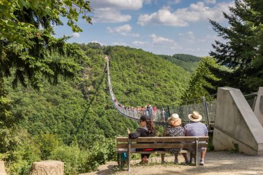 People sitting on a bench at the Geierlay suspension bridge in Germany clipart