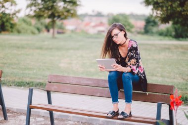 Tablet bilgisayarla bankta oturan genç bir kadın