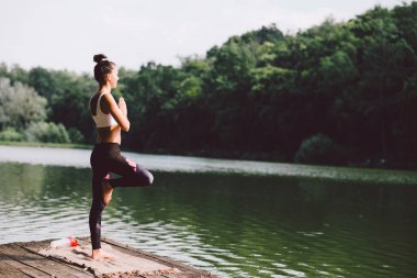 Nehir kıyısında yoga yapan genç bir kadın.