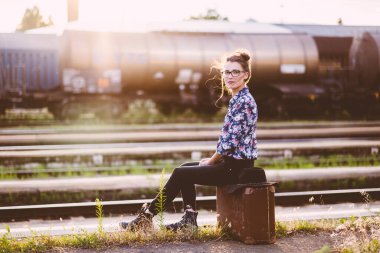 Bavullu genç bir kadın demiryolunda oturuyor.