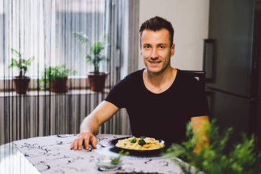 Genç adam mutfakta salata yiyor.