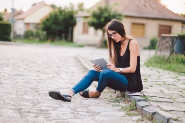 Genç bir kadın bankta oturuyor ve tablet kullanıyor.