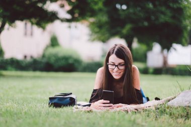 Genç bir kadın akıllı telefon kullanarak yaz parkında dinleniyor.