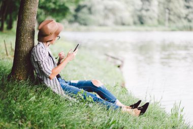 Genç bir kadın akıllı telefon kullanarak yaz parkında dinleniyor.
