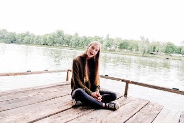 Kız iskelede oturuyor ve kameraya bakıyor.