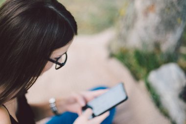 Genç bir kadın akıllı telefon kullanarak yaz parkında dinleniyor.