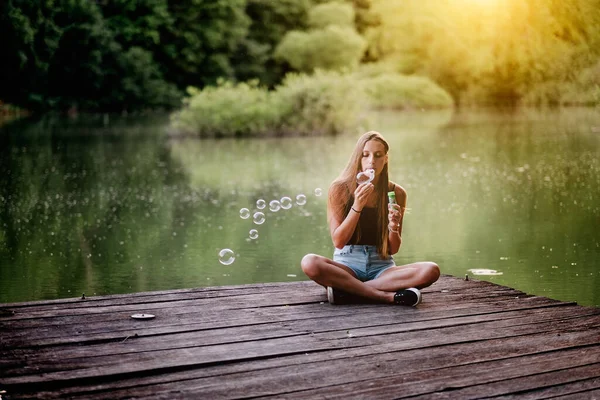 湖の桟橋に座っている若い女性は — ストック写真